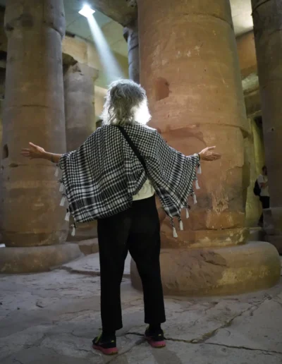 Ajarona standing in ancient Egyptian corridor with light shining through stone wall onto her face